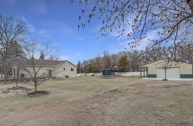 view of yard featuring a garage, a trampoline, an outdoor structure, and fence