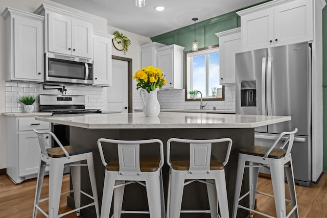 kitchen with appliances with stainless steel finishes, a center island, white cabinets, and decorative light fixtures