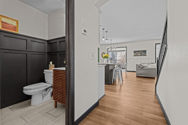 hallway with a decorative wall, light wood finished floors, and an inviting chandelier