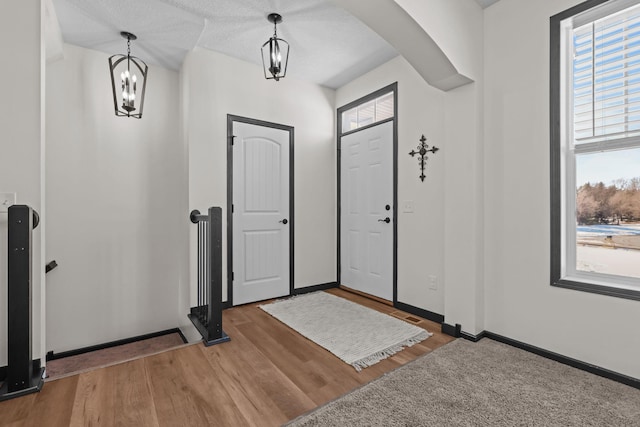 foyer with a chandelier, arched walkways, baseboards, and wood finished floors