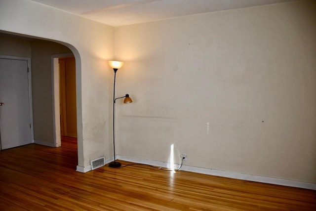 spare room featuring arched walkways, wood finished floors, visible vents, and baseboards