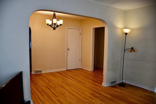 empty room featuring arched walkways, light wood finished floors, visible vents, and baseboards