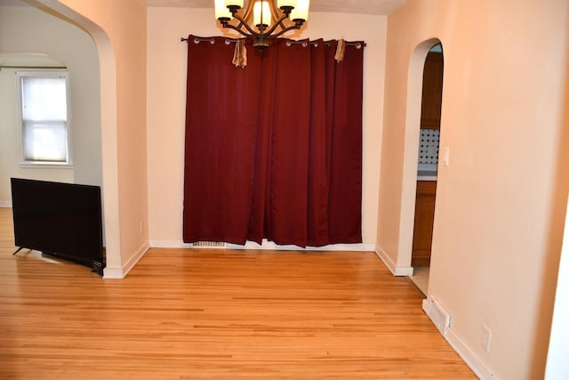 unfurnished dining area with light wood finished floors, baseboards, arched walkways, and a notable chandelier