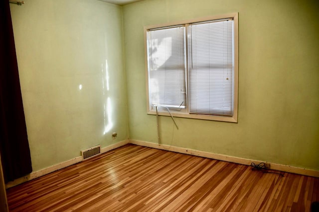 spare room featuring light wood finished floors, baseboards, and visible vents