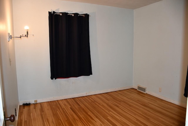 empty room with wood finished floors, visible vents, and baseboards