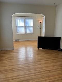 unfurnished living room featuring light wood-style floors, baseboards, and arched walkways