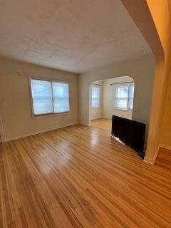 unfurnished living room with arched walkways and light wood-style flooring