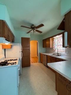 kitchen featuring brown cabinets, white gas stove, light countertops, a sink, and ventilation hood