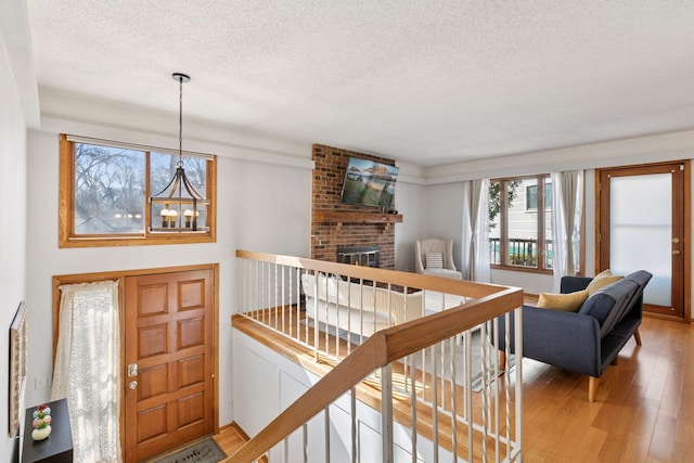 entrance foyer with light wood-style floors, a brick fireplace, a notable chandelier, and a textured ceiling