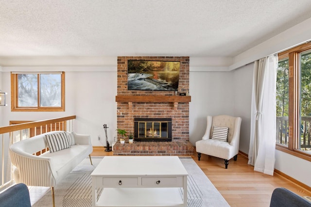 living room featuring light wood-style flooring, a fireplace, baseboards, and a textured ceiling