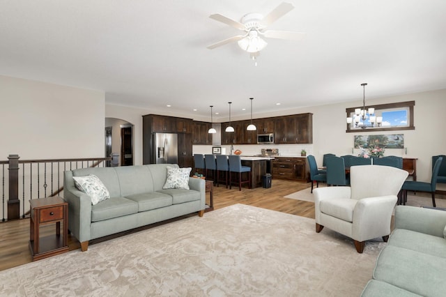 living room featuring ceiling fan with notable chandelier and light hardwood / wood-style flooring