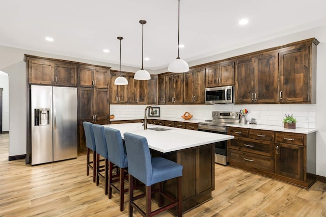 kitchen featuring hanging light fixtures, dark brown cabinetry, stainless steel appliances, an island with sink, and sink