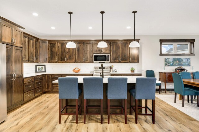 kitchen featuring dark brown cabinetry, stainless steel appliances, hanging light fixtures, and an island with sink