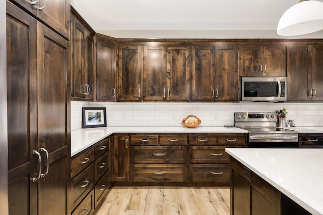 kitchen featuring light wood-type flooring, appliances with stainless steel finishes, dark brown cabinetry, and decorative backsplash