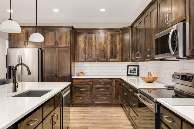 kitchen featuring appliances with stainless steel finishes, sink, pendant lighting, light hardwood / wood-style floors, and dark brown cabinets