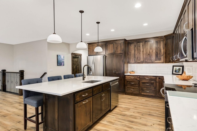 kitchen featuring appliances with stainless steel finishes, sink, dark brown cabinets, and a kitchen island with sink