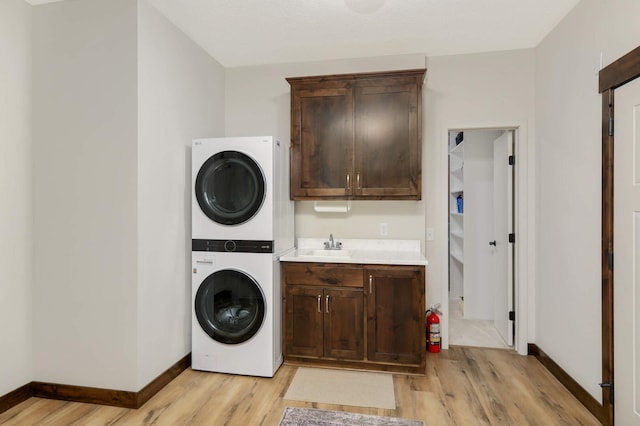 laundry room with sink, light wood-type flooring, stacked washer / drying machine, and cabinets