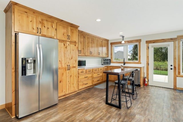 kitchen with stainless steel appliances, a kitchen bar, wood-type flooring, and light brown cabinets