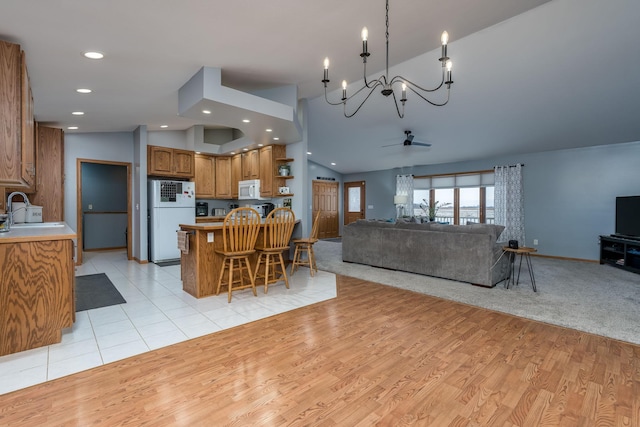 kitchen featuring a kitchen breakfast bar, white appliances, lofted ceiling, ceiling fan with notable chandelier, and sink