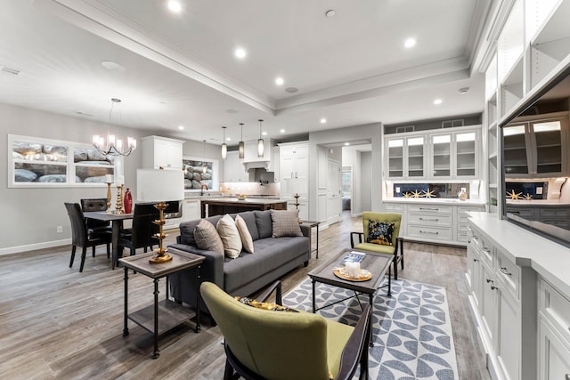 living room with a tray ceiling, hardwood / wood-style floors, crown molding, and a chandelier