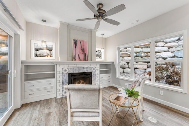 living room featuring a tile fireplace, light hardwood / wood-style floors, and ceiling fan