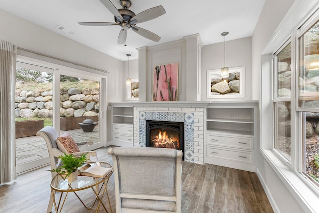 living room with ceiling fan, light hardwood / wood-style floors, a tile fireplace, and a healthy amount of sunlight