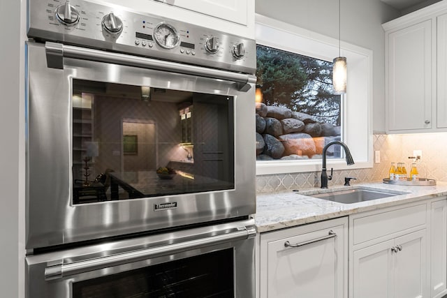 kitchen with white cabinetry, decorative light fixtures, sink, tasteful backsplash, and light stone counters