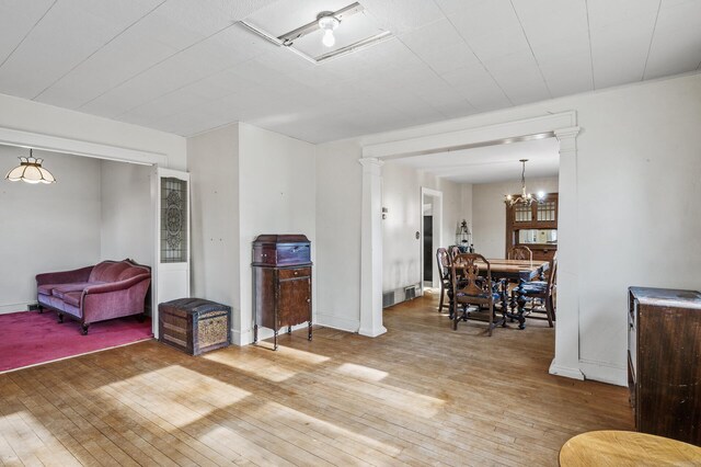 living room featuring light wood-style floors, a chandelier, baseboards, and ornate columns