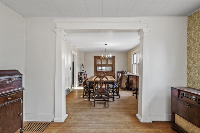 dining space with a chandelier, baseboards, light wood-style flooring, and ornate columns