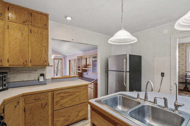 kitchen featuring a sink, light countertops, freestanding refrigerator, wallpapered walls, and pendant lighting