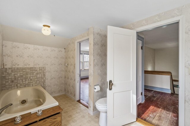 bathroom featuring baseboards, a tub with jets, toilet, and wallpapered walls