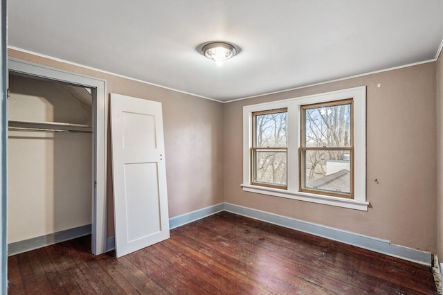 unfurnished bedroom featuring dark wood-type flooring, a closet, crown molding, and baseboards