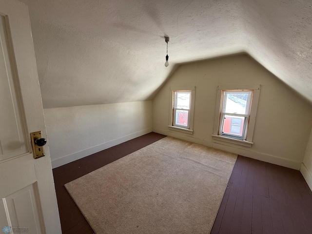 bonus room with dark wood-type flooring, a textured ceiling, and lofted ceiling