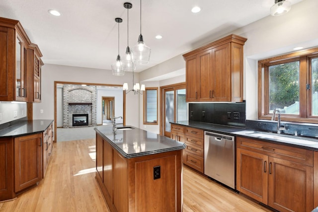 kitchen with an island with sink, a brick fireplace, hanging light fixtures, sink, and dishwasher