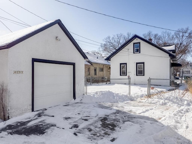 view of snow covered exterior with a detached garage, fence, and stucco siding