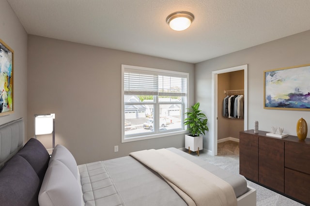 bedroom with a closet, a textured ceiling, a spacious closet, and light colored carpet