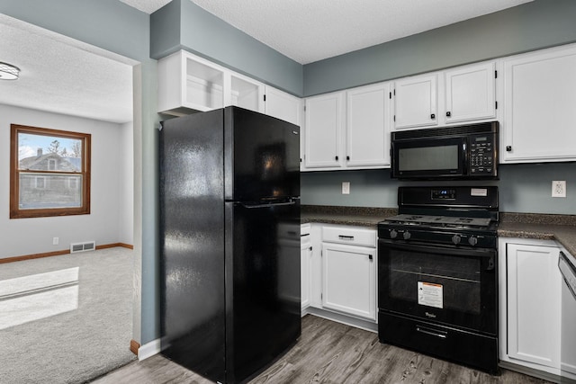 kitchen with white cabinetry, a textured ceiling, black appliances, and hardwood / wood-style floors