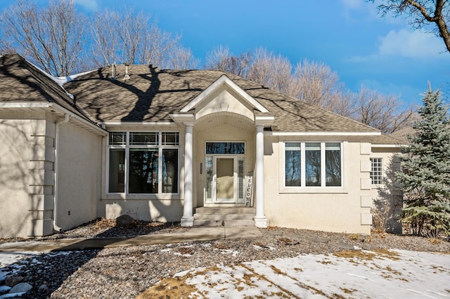 view of exterior entry featuring a shingled roof and stucco siding