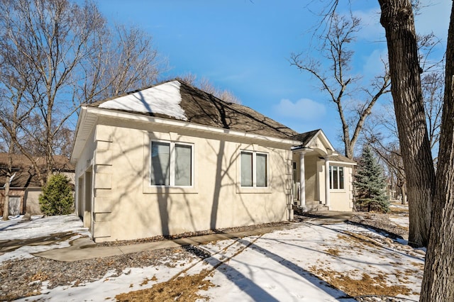 view of snowy exterior featuring stucco siding and roof with shingles