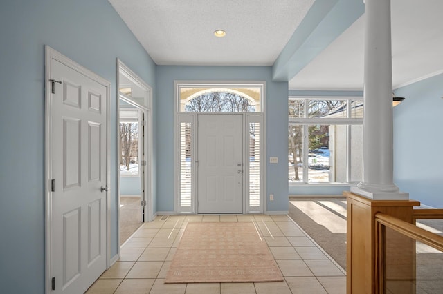 entrance foyer featuring light tile patterned flooring, light colored carpet, a textured ceiling, and decorative columns