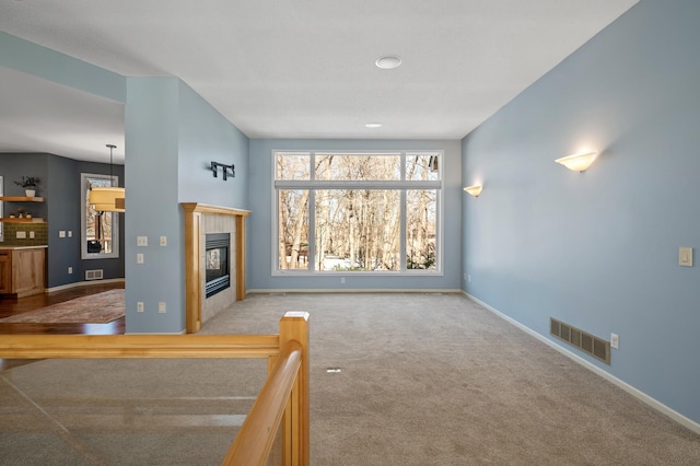 unfurnished living room with visible vents, a tile fireplace, carpet, and baseboards