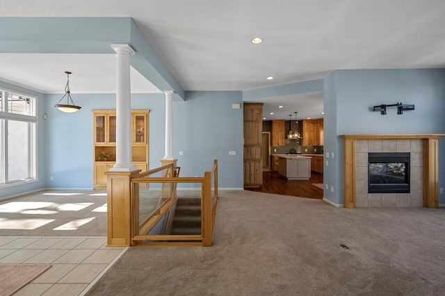 unfurnished living room with a tiled fireplace, light colored carpet, and decorative columns