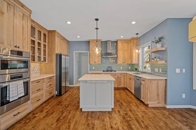 kitchen with light brown cabinets, a sink, stainless steel appliances, light countertops, and wall chimney exhaust hood