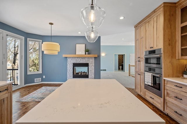 kitchen featuring light brown cabinets, visible vents, a tile fireplace, light countertops, and double oven