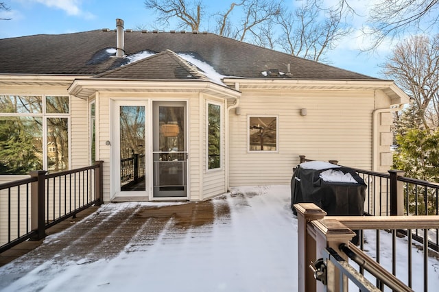 snow covered rear of property with a shingled roof