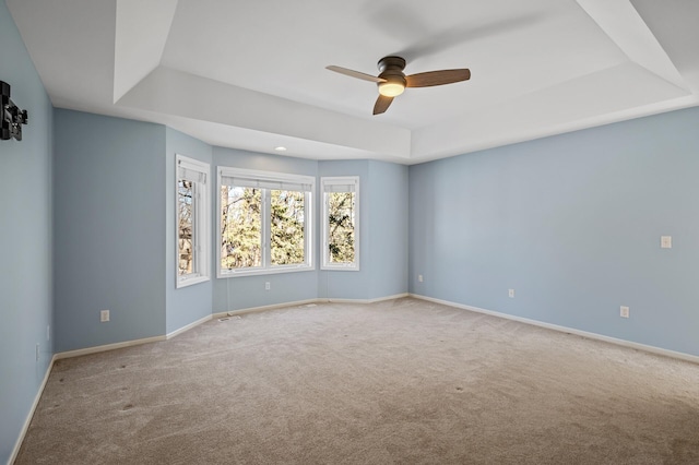 carpeted spare room with ceiling fan, baseboards, and a tray ceiling