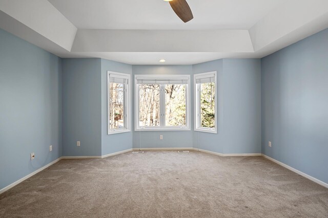 carpeted empty room featuring a ceiling fan, a raised ceiling, and baseboards