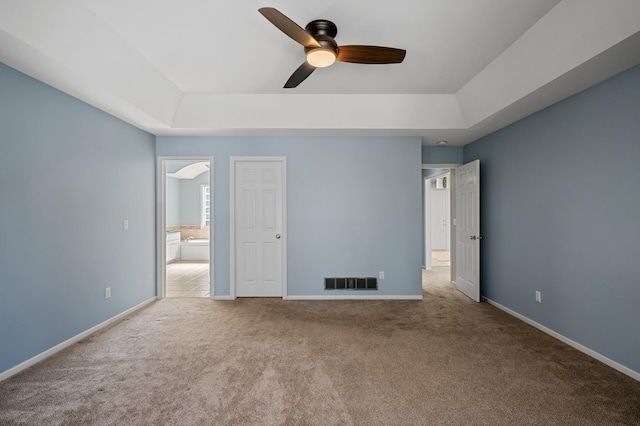 unfurnished bedroom with visible vents, a raised ceiling, carpet, and baseboards