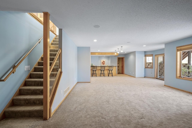 basement featuring visible vents, a textured ceiling, baseboards, light colored carpet, and stairs