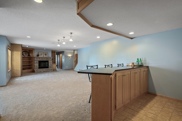 kitchen featuring light carpet, a breakfast bar, a textured ceiling, a peninsula, and a fireplace